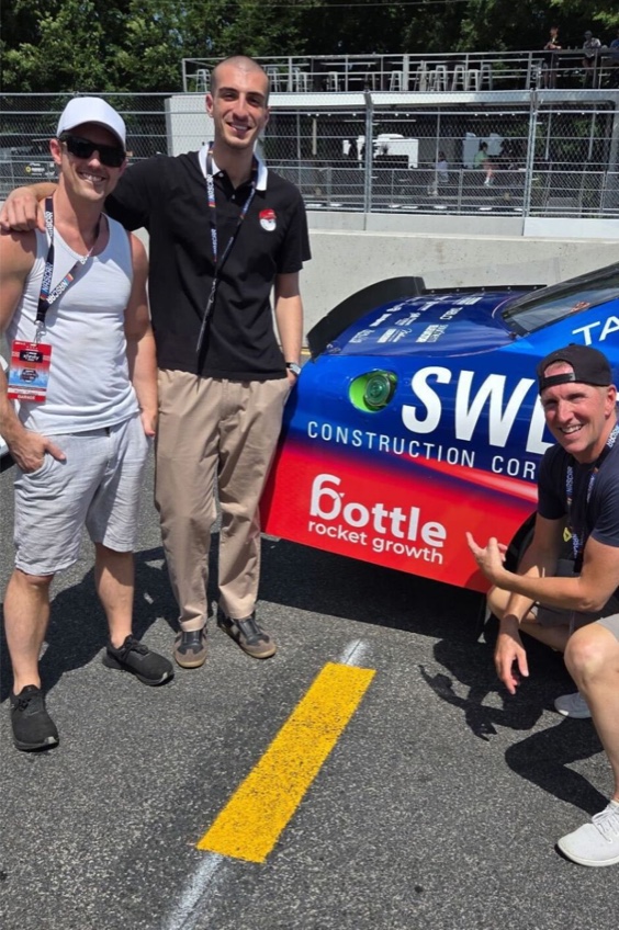 Mike Cubberly, Steve Cubberly, and Zuka beside the race car and its Bottle Rocket Growth logo